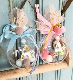 two clear glass ornaments with pink and blue pom poms on them, hanging from a wooden shelf