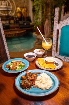 a wooden table topped with blue plates filled with food next to a glass of orange juice