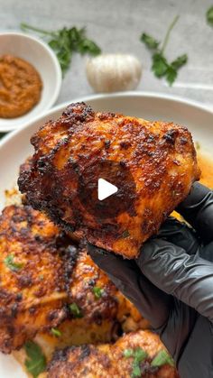 a person in black gloves holding up some food on a white plate with sauces