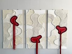 three pieces of art with red and white designs on them, hanging on the wall