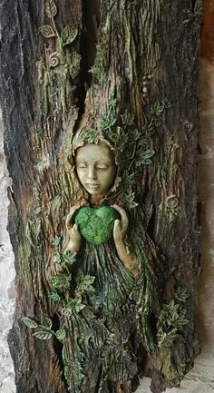 a statue of a woman holding a green heart in front of a piece of wood