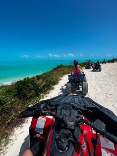 people riding four wheelers on the beach next to the ocean with clear blue skies