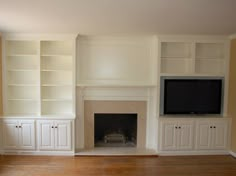 an empty living room with built - in bookshelves and a tv above the fireplace