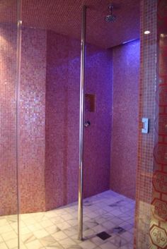 a walk in shower sitting next to a purple tiled wall and floor with lights on it