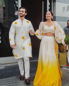 two people dressed in white and yellow outfits walking down the street with flowers on them