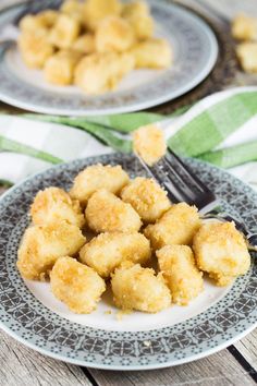 two plates filled with tater tots on top of a wooden table next to a fork