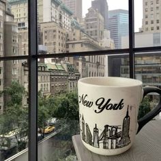 a coffee cup sitting on top of a window sill in front of a cityscape