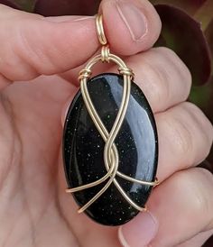 a person holding a black and gold pendant in their left hand, with the wire wrapped around it