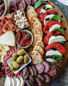 an assortment of meats and cheeses on a wooden platter with olives