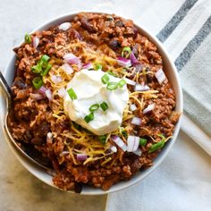 a bowl filled with chili and sour cream on top of a white towel next to a spoon