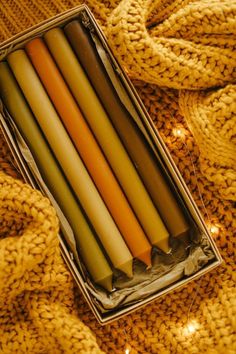 four candles in a metal box on a knitted surface with lights around them and wrapped in yellow yarn