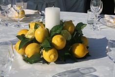 a white table topped with lots of lemons next to a candle and plates filled with silverware