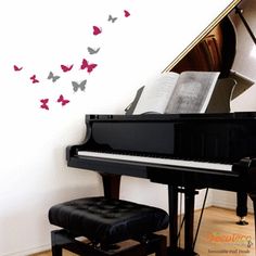 a black piano in front of a white wall with butterflies on it and a stool next to it