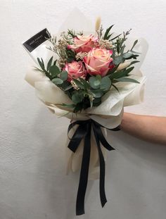 a bouquet of pink roses and greenery wrapped in white paper with a black ribbon