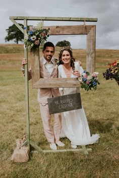 a bride and groom standing in front of a wooden frame holding a sign that says we miss you