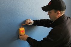 a man is painting the wall with blue paint and an orange box next to him