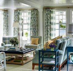 a living room filled with lots of furniture next to two windows covered in blue curtains