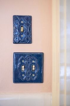 two blue light switch plates mounted to the side of a pink wall with white trim