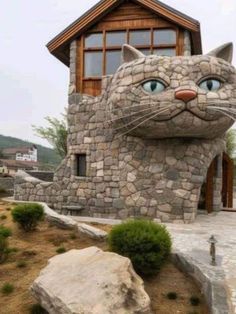 a cat made out of rocks sitting in front of a house