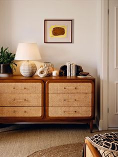 a lamp is on top of a wicker dresser in a room with white walls