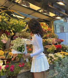 a woman is looking at flowers in a flower shop while wearing a short white dress