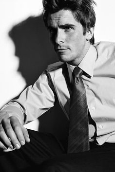 black and white photograph of a man wearing a shirt and tie sitting on a chair