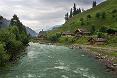 a river running through a lush green hillside covered in forest next to small wooden houses