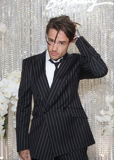 a man in a suit and tie standing next to a wall with flowers on it