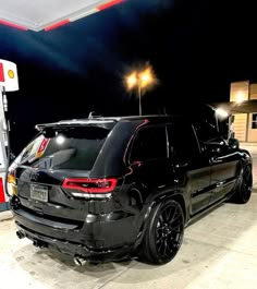 a black jeep is parked in front of a gas station at night with its lights on