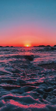 the sun is setting over the ocean with waves coming in to shore and sand on the beach