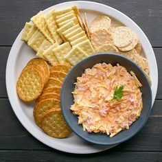 a plate full of crackers, crackers and dip on a white plate with a blue bowl