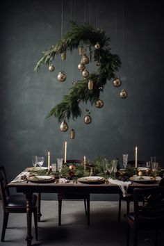 a dining room table set for christmas with ornaments hanging from the ceiling and candles lit