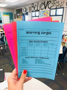 a person holding up three blue and pink learning target posters in front of a classroom