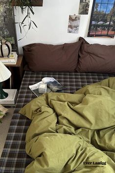 an unmade bed in a bedroom with green sheets and pillows on the floor next to a lamp