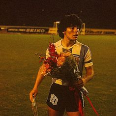 a young man holding a bouquet of flowers in his hands on a soccer field at night