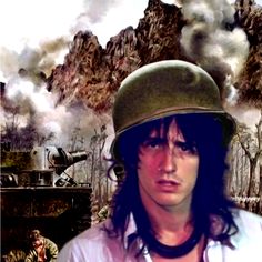 a man with long hair wearing a helmet and looking at the camera while standing in front of a tank