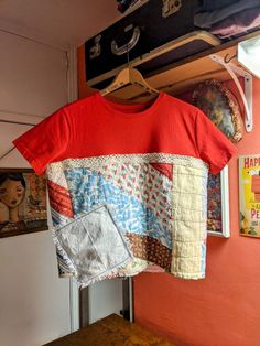 a red shirt hanging on a clothes rack next to a wall with pictures and other items