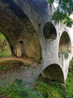 an old stone bridge with arches over it and a person sitting on the bench below