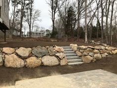 a stone wall with steps leading up to it in front of a house and trees