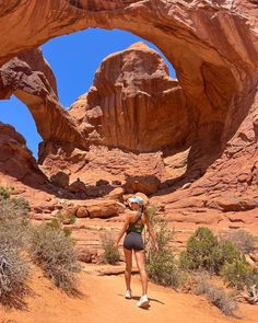 a woman is walking through the desert in front of an arch shaped rock formation,