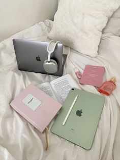 an open laptop computer sitting on top of a bed next to two notebooks and headphones