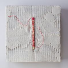 a piece of white paper with red thread on it and a needle in the middle