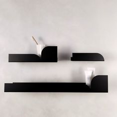 two black shelves with toothbrushes and lotion in them against a white wall