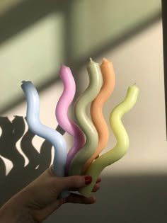 a hand holding five different colored candles in the shape of wavy waves on a white wall