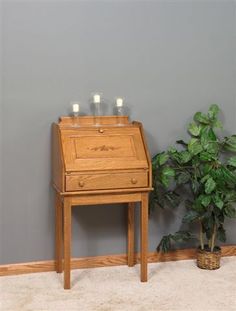 a small wooden desk next to a potted plant on the floor in front of a gray wall