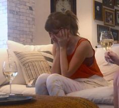 two women sitting on a couch with wine glasses in their hands and one holding her head