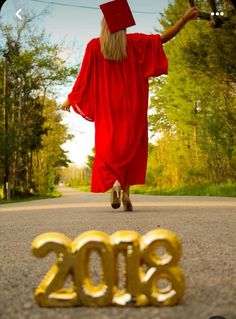 a woman in a graduation gown is walking down the street with her arms out and she's wearing a red cap and gown