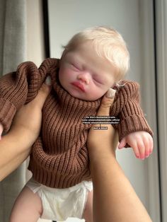 a woman holding a baby wearing a brown sweater and white diaper on it's chest