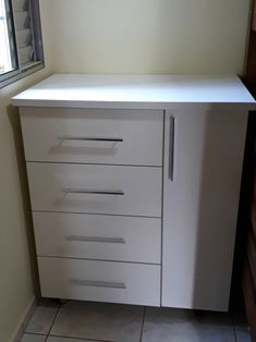 a white cabinet sitting in the corner of a room next to a window and tiled floor