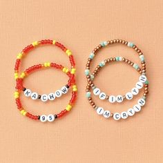 three bracelets with words on them sitting on top of a pink surface and one has an orange bead around it